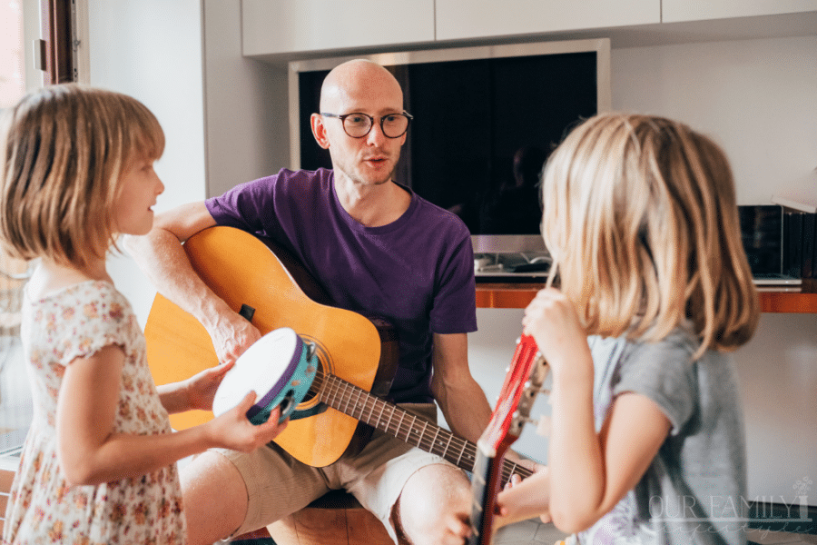 father teaching daughters how to play guitar