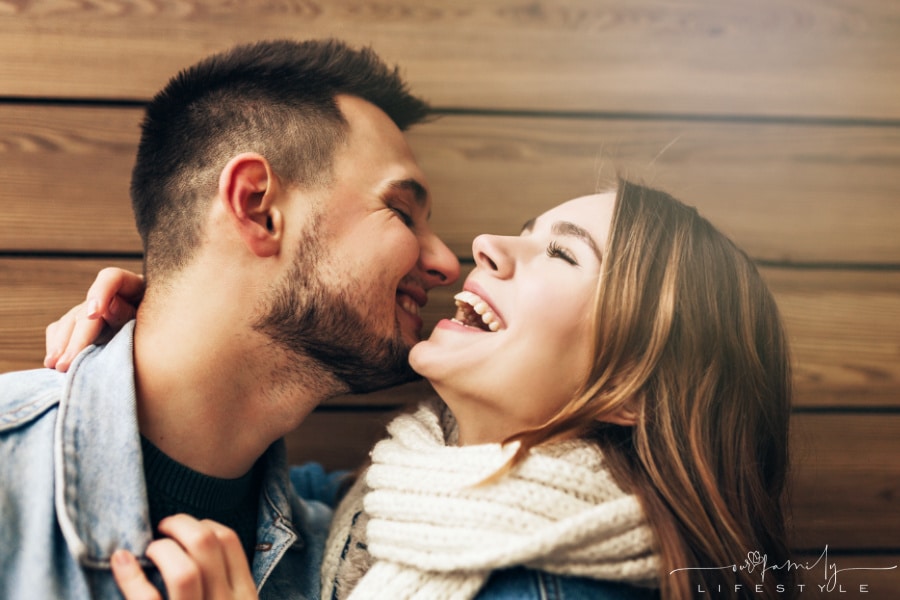 brunette-laughing-with-husband-expressing-love-while-posing-in-front-of-wooden-wall