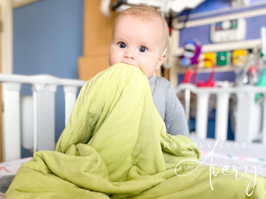 blue eyed baby holding green bamboo blanket in hospital bed