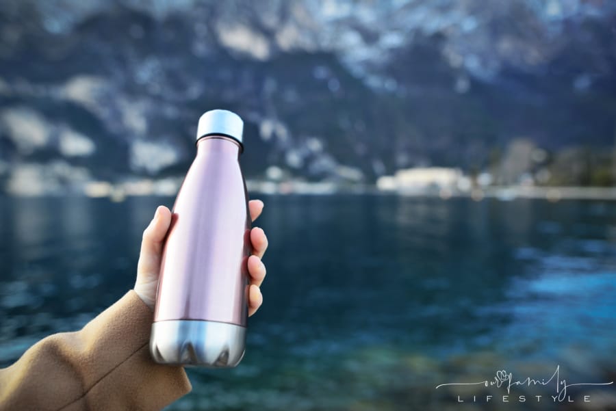 female-hand-holding-reusable-steel-thermo-bottle-background-clear-water-lake