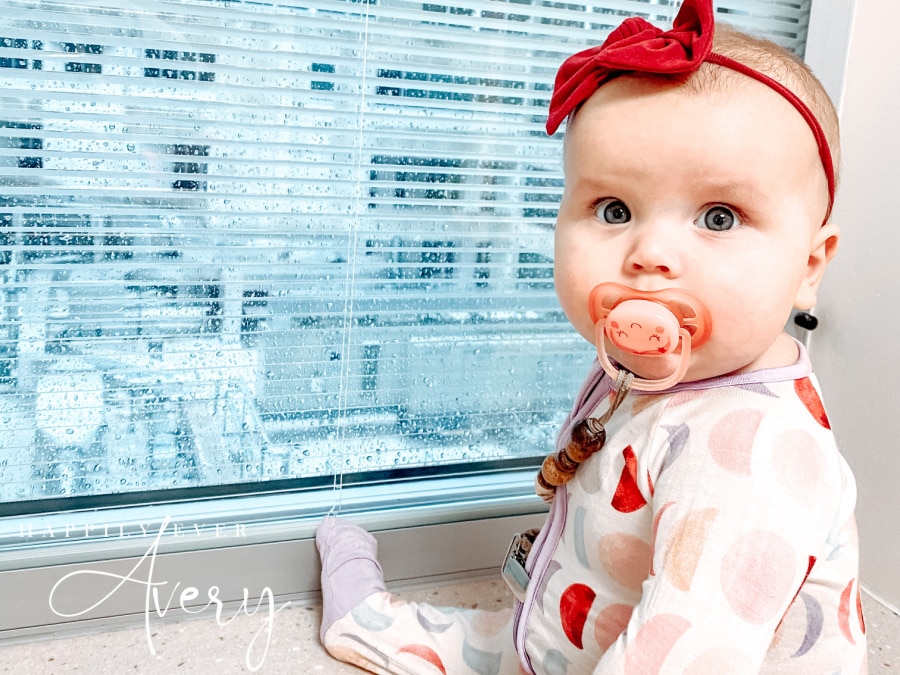 infant with red bow in her hair sitting in front of rain splashed hospital window
