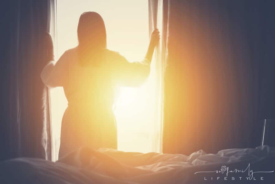 woman opening black out curtains to let sunshine in