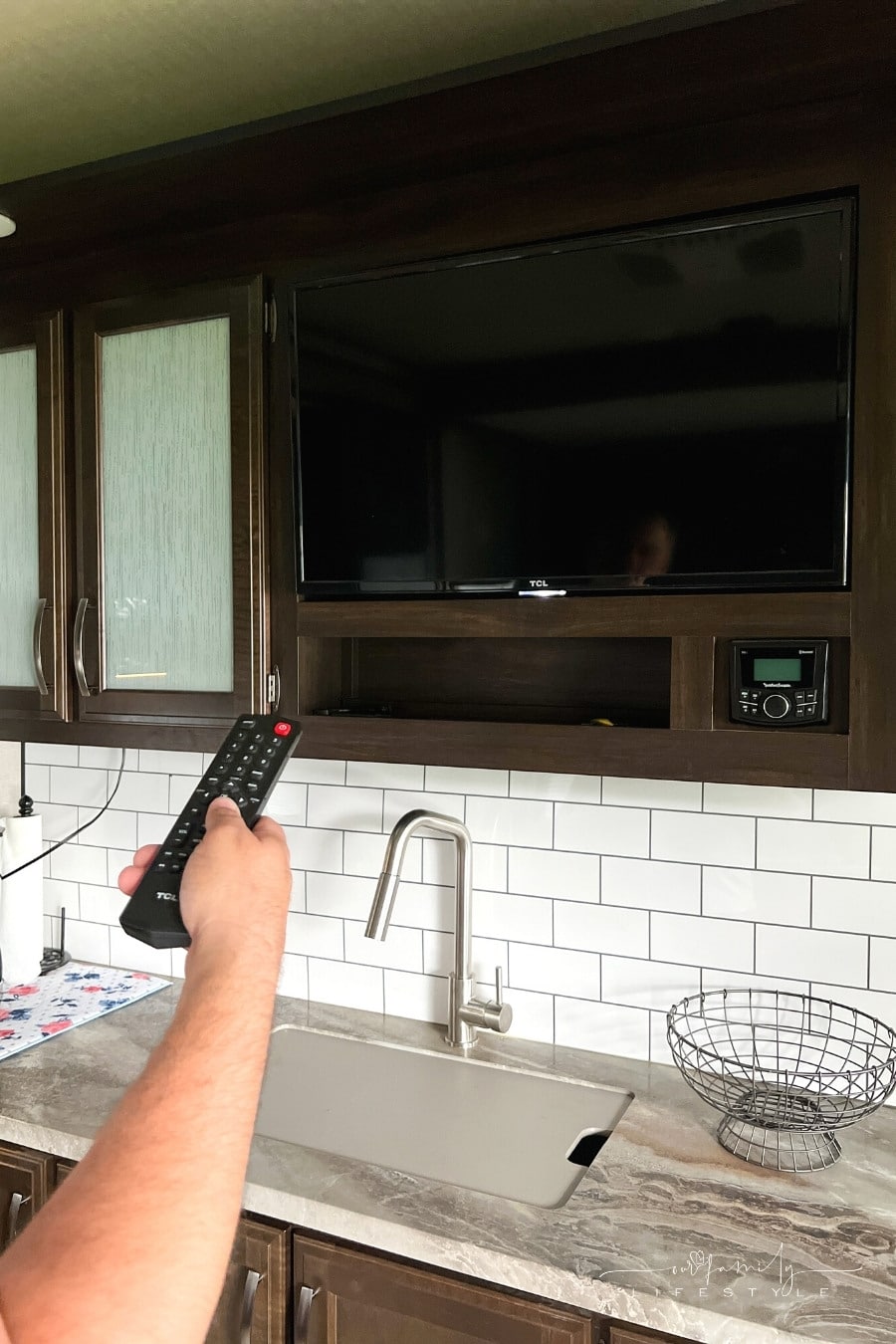 hand holding remote control aimed at tv in rv trailer kitchen