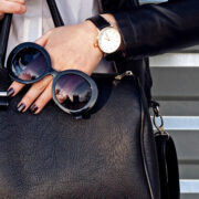 woman holding black handbag with sunglasses and jewelry on hand