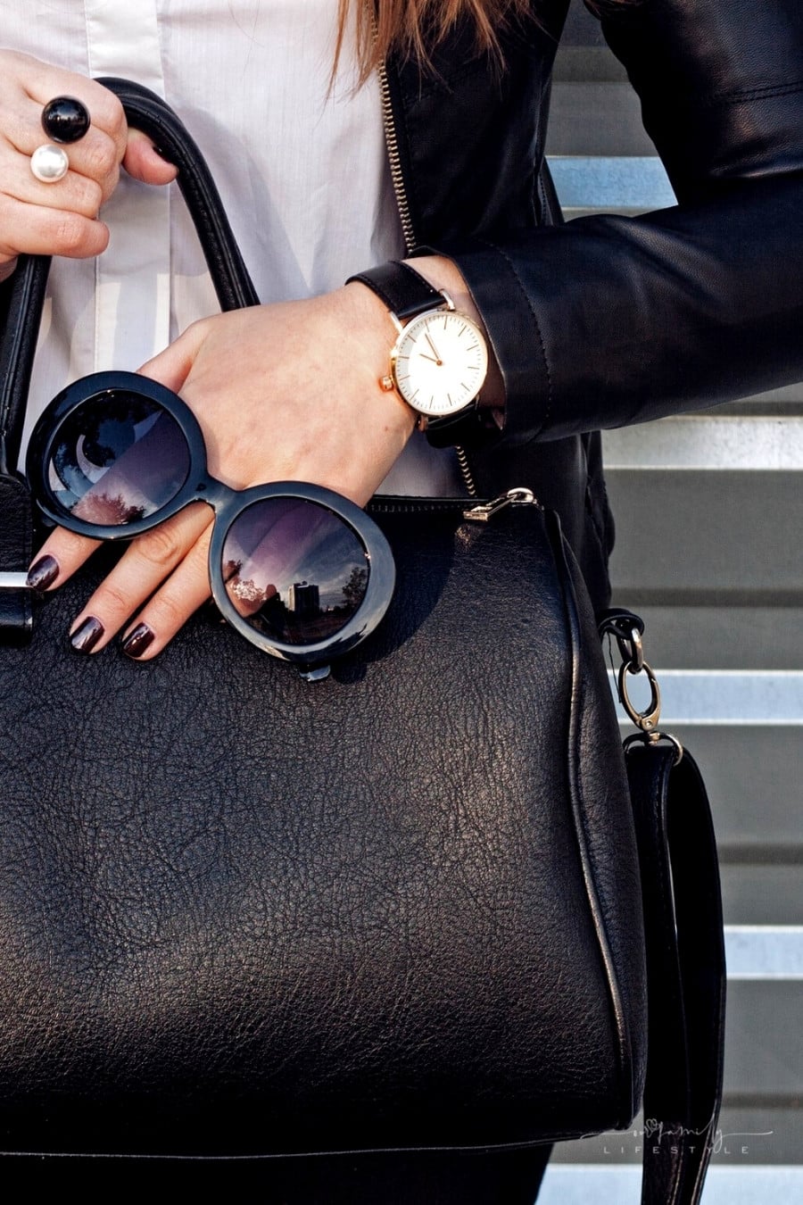 woman holding black handbag with sunglasses and jewelry on hand