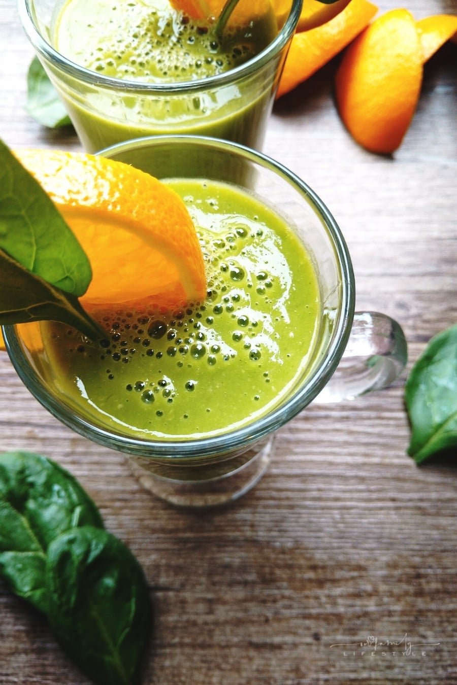 green smoothie with spinach, orange, and mango around the glass