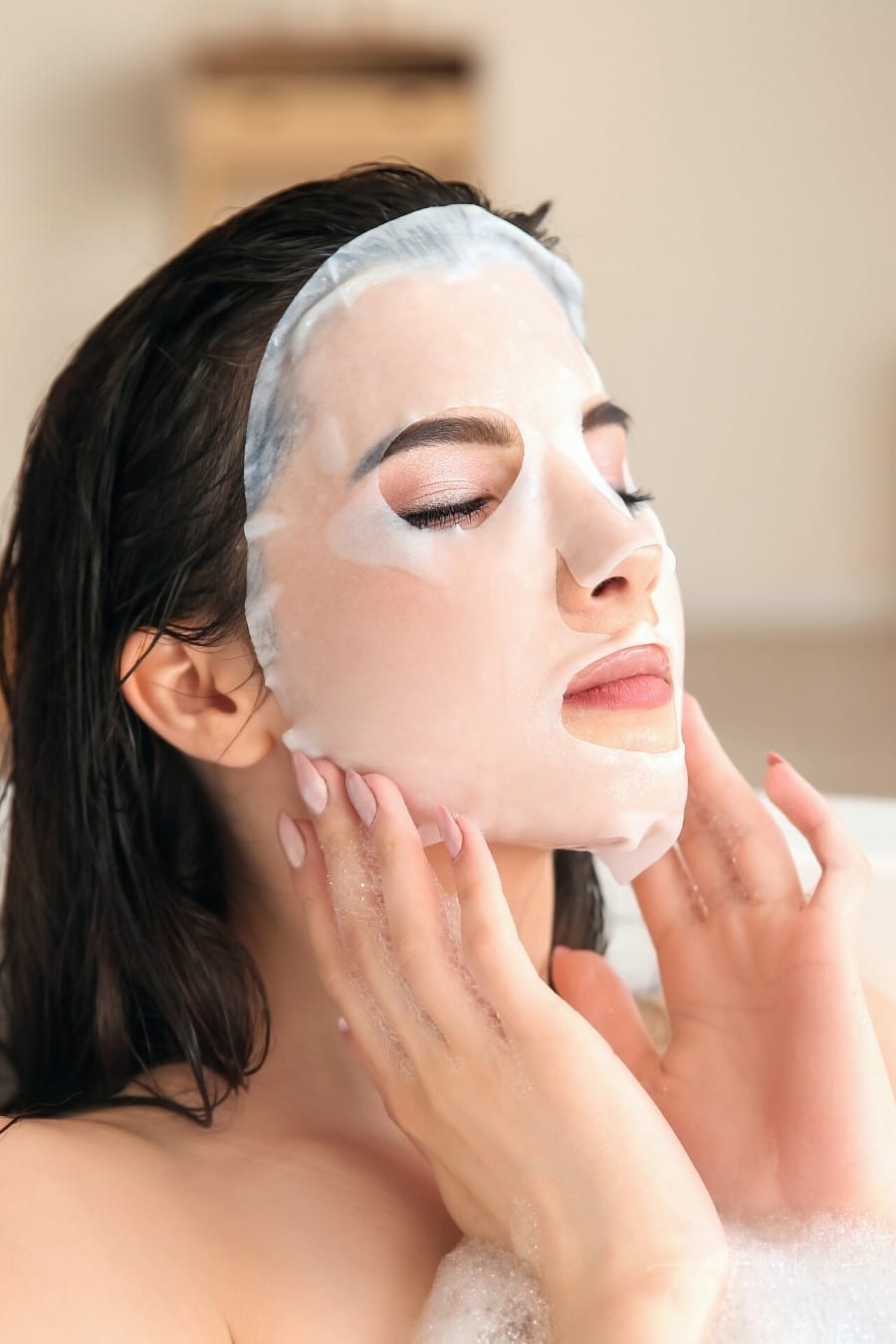 woman wearing facial sheet mask in a bathtub