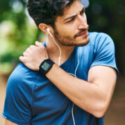 sporty young man holding his shoulder after exercising outdoors