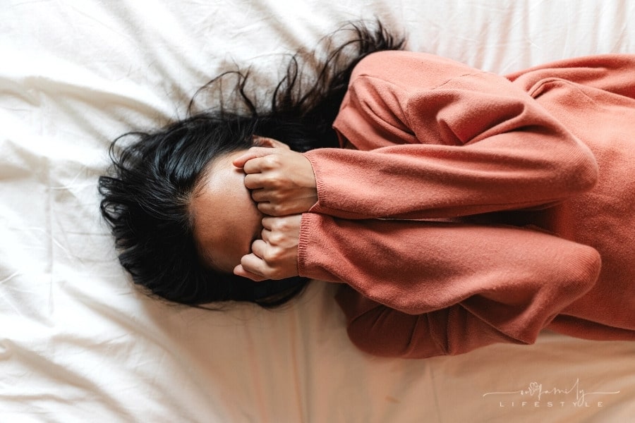 top view of a woman crying while covering her face with her hands in bed