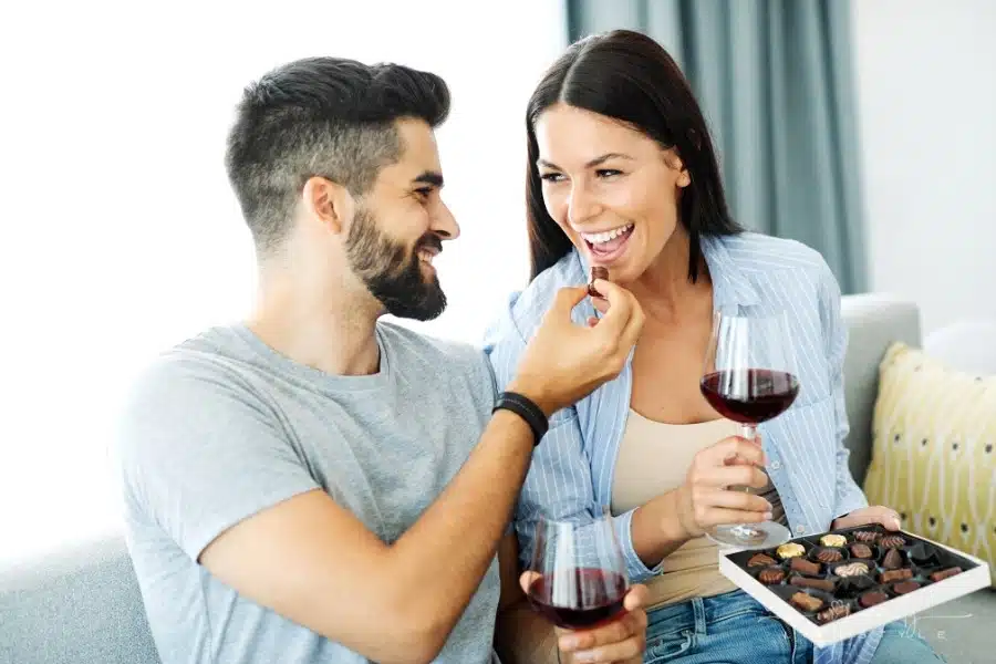 young couple eating chocolates and drinking wine together on couch