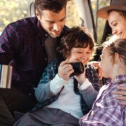 happy young family sitting in back of car with camera