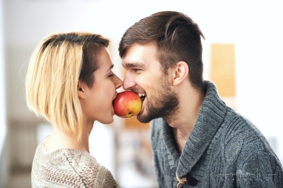young couple holding an apple between them with their teeth