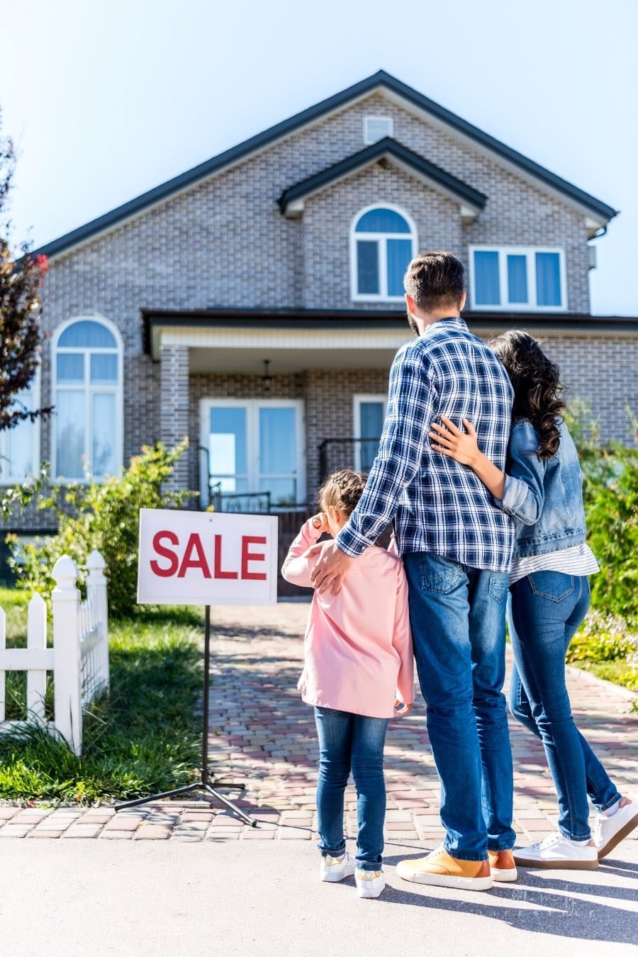 mom, dad and young daughter in front of new house with for sale sign