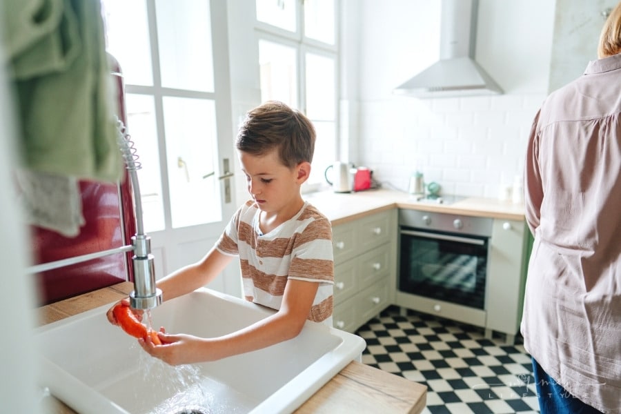 little boy helping wash vegetables in the kitchen