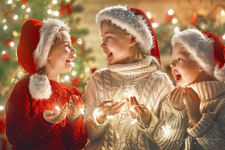 three children in Santa hats holding a string of lights while smiling