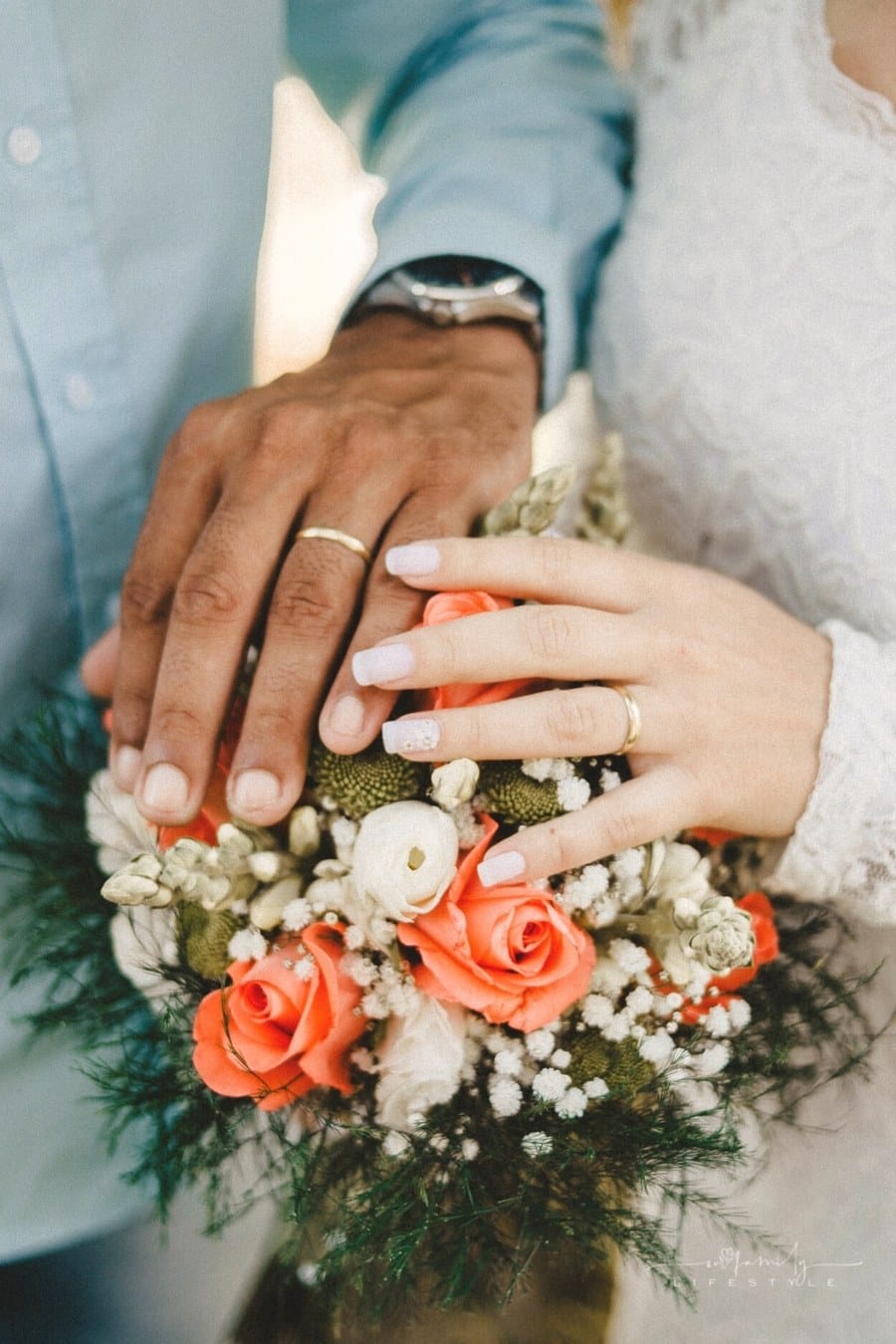 bride and groom's hands with wedding bands over bouquet