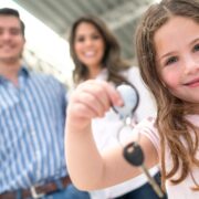 young girl holding out keys to new family car with parents in background