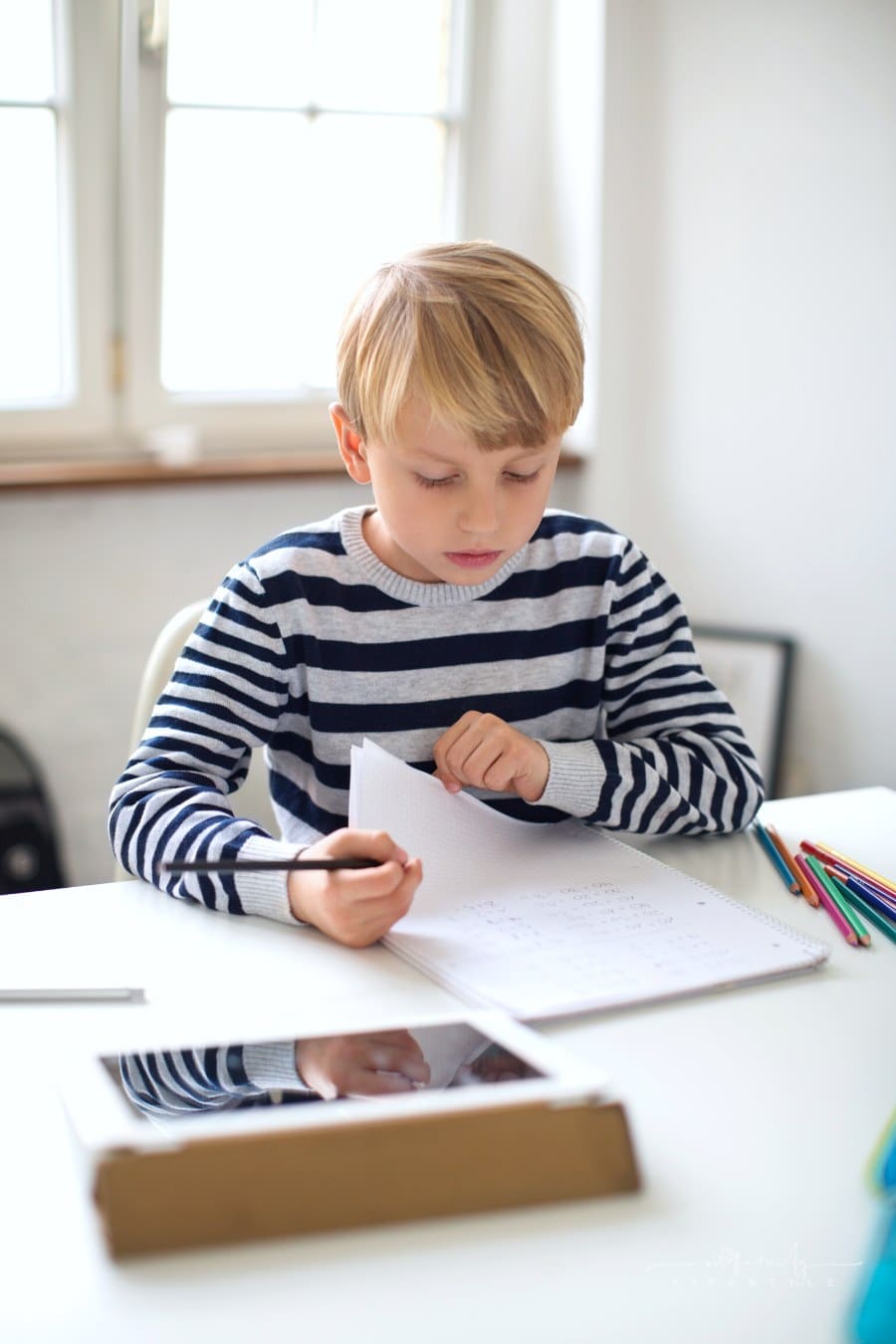 young boy sitting at white desk doing homework
