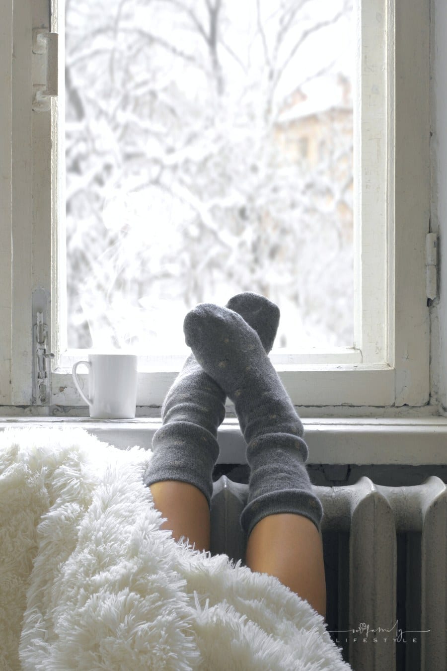 woman's legs and feet under shaggy blanket with hot coffee on windowsill