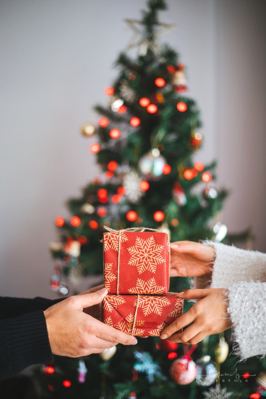 man and woman's hands exchanging gifts in front of a Christmas tree