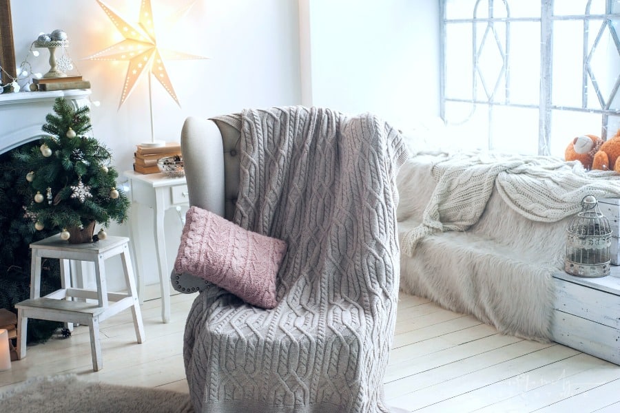 gray wingback chair with cable knit blanket and pink pillow on it with Scandinavian background