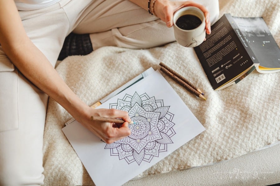 female drawing in adult coloring book while holding a cup of coffee