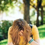 depressed teen girl sitting on sidewalk and holding her head in her hands
