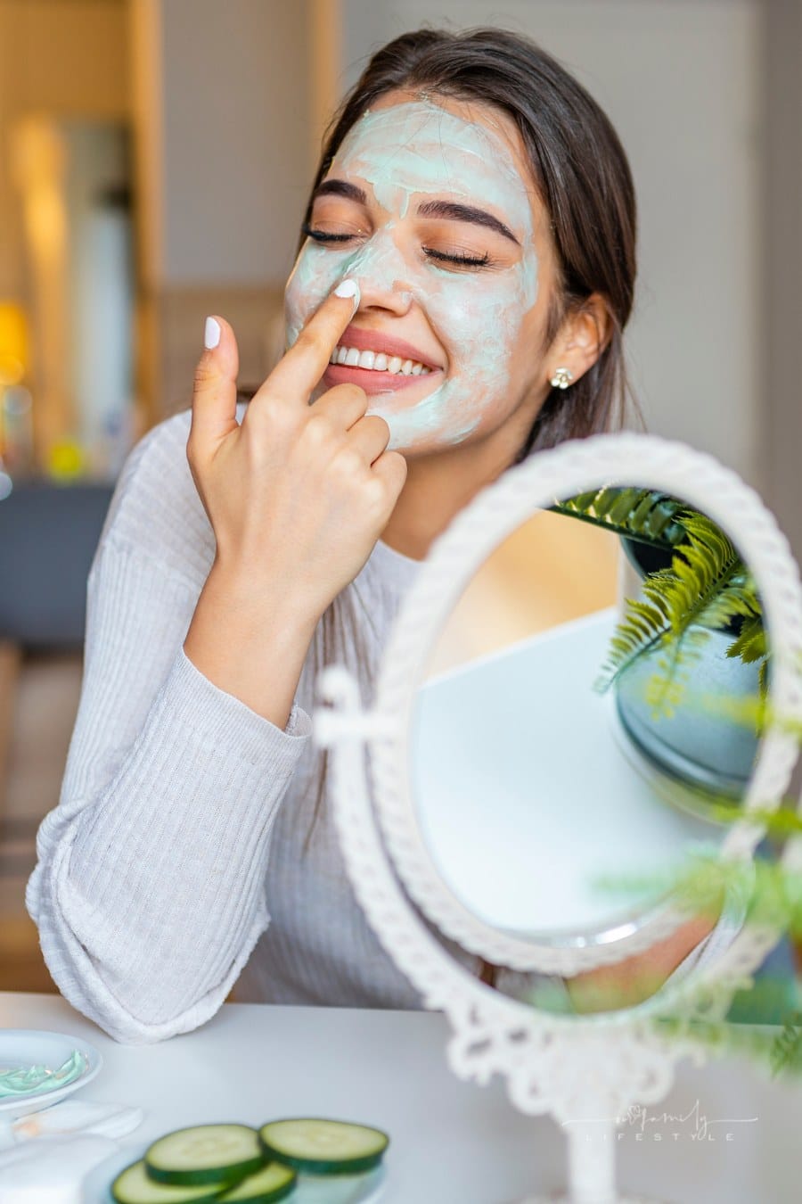 woman putting a green face mask on in front of table mirror