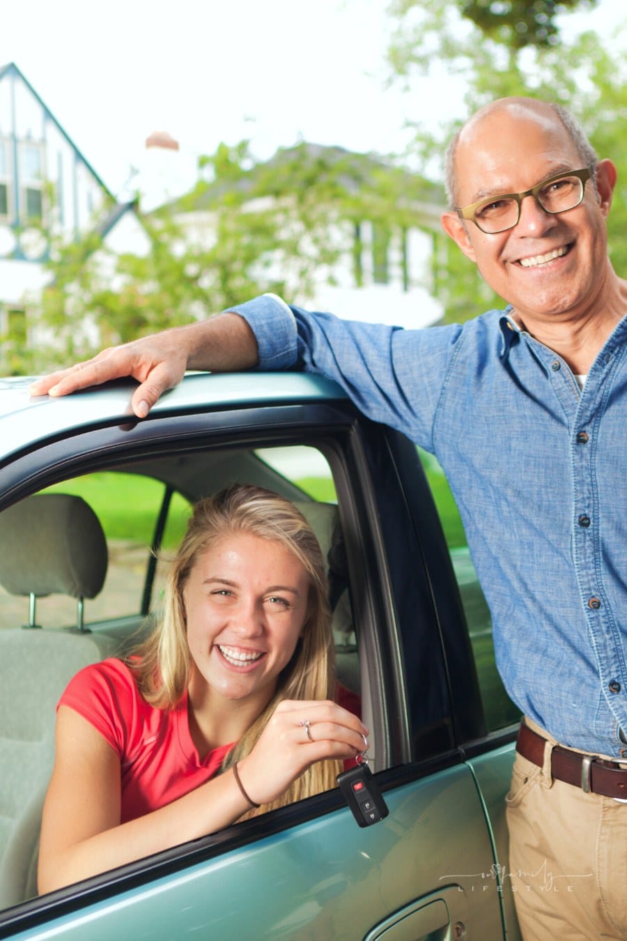 father standing beside driver's side window with teen daughter holding keys to the car and smiling