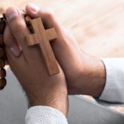 man's praying hands holding a rosary over a Bible