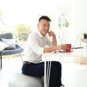 Happy young businessman sitting on fitness ball in office. Workplace exercises