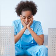 tired nurse sitting in waiting room chair with hands in head