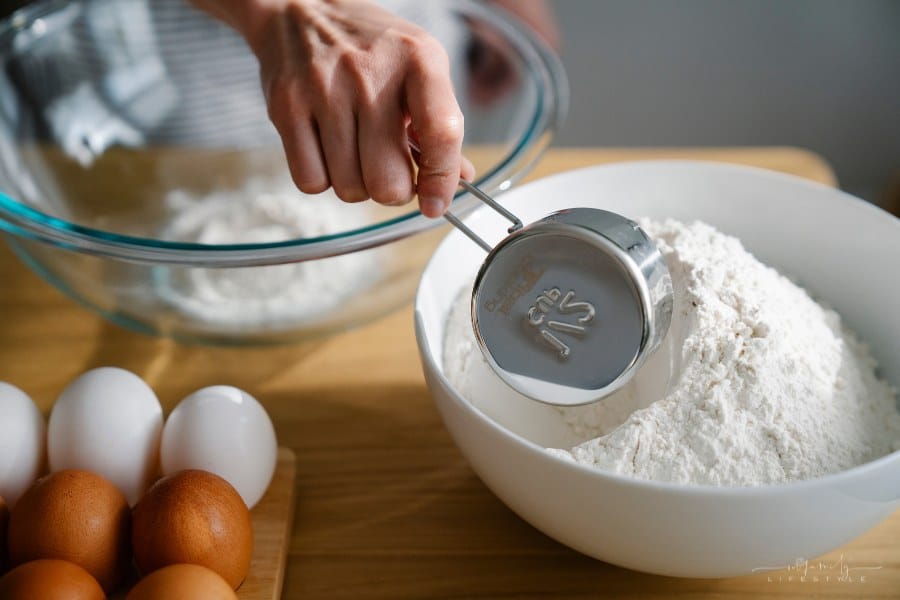 woman's hands measuring flour out of a bowl with a metal measuring cup