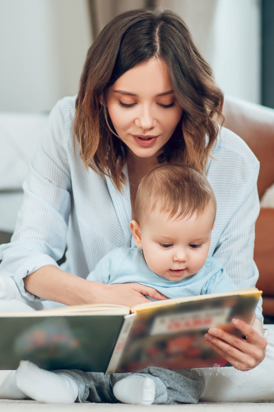 attentive mother reading book to small child sitting together on floor at home