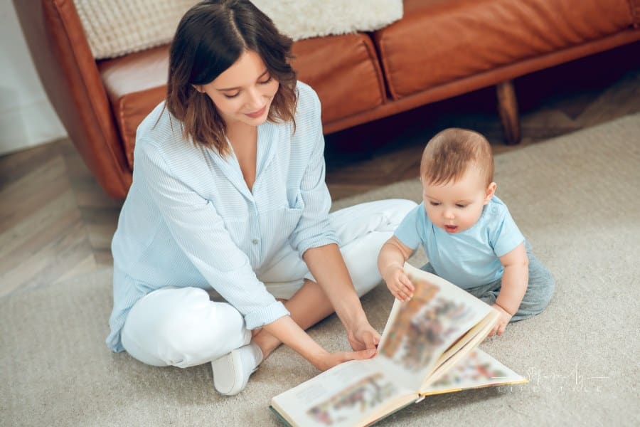 attentive mother reading book to small child sitting together on floor at home