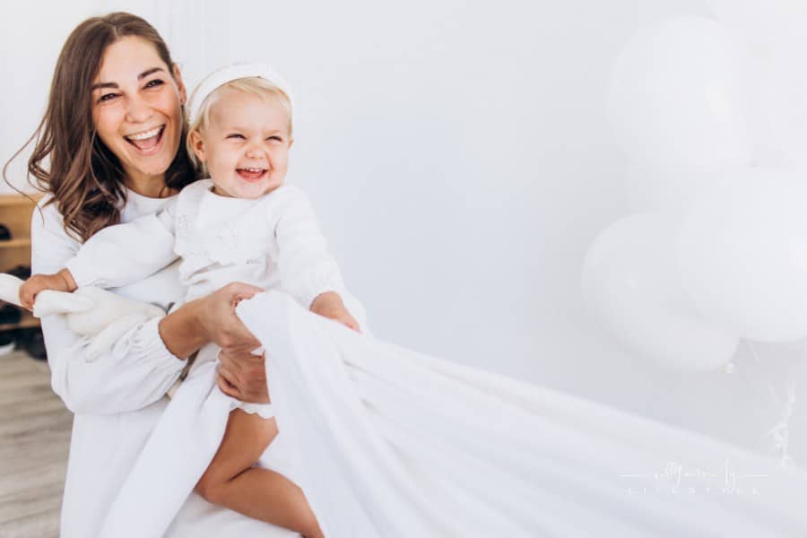 Mom and daughter play with a sheet. The baby and mom are smiling. Happy family.