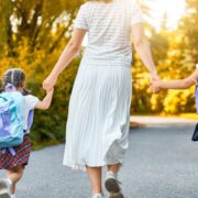 mother wearing long white skirt walking her three daughters to school with backpacks on