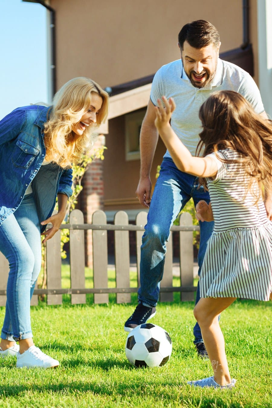 Little daughter playing soccer with her parents outside