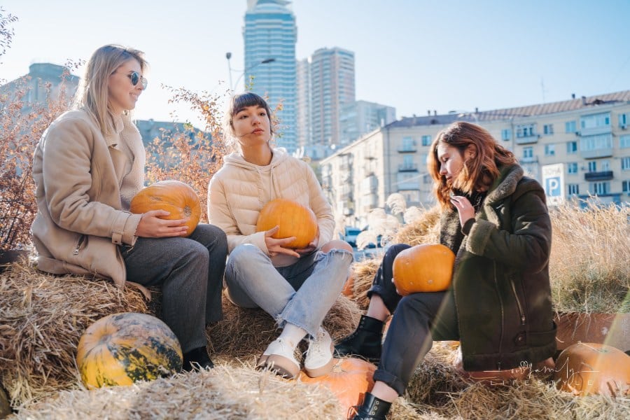 women Holding Pumpkins while wearing fall outerwear with City in the Background