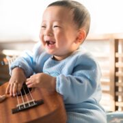 baby laughing while holding a small guitar