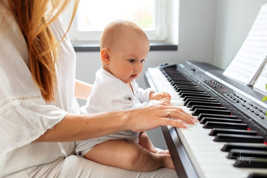 woman playing piano with baby on her lap; baby has hands on keys of piano