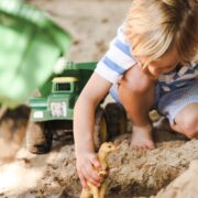 Preschool boy playing with diggers and trucks in sandpit