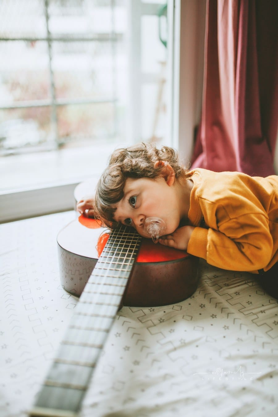 Portrait Of a Young Child Laying on a Guitar At Home with a Pacifier in his mouth