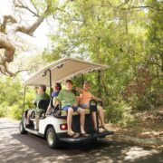 family riding on golf cart along tree-shadowed trail