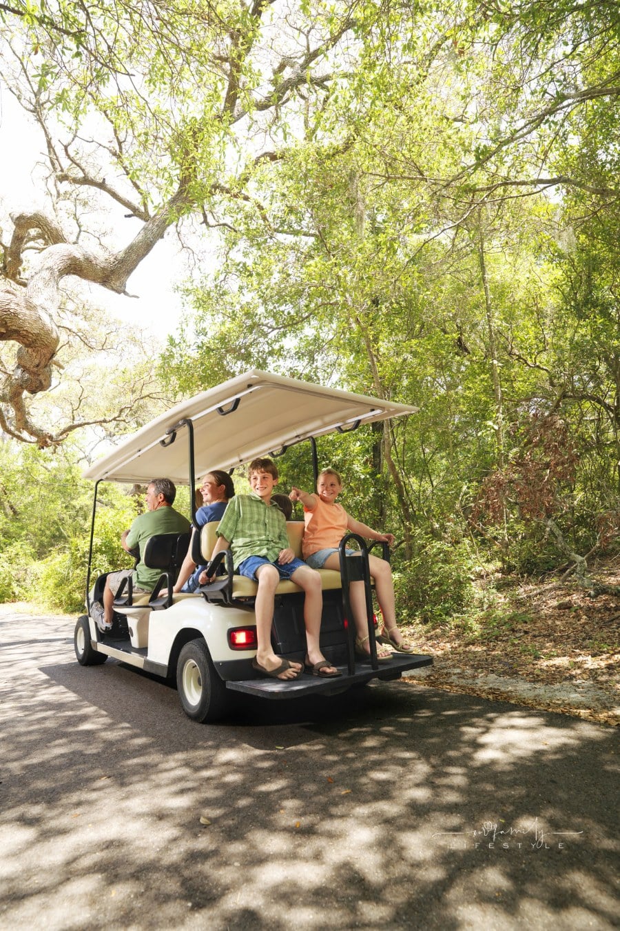 family riding on golf cart along tree-shadowed trail