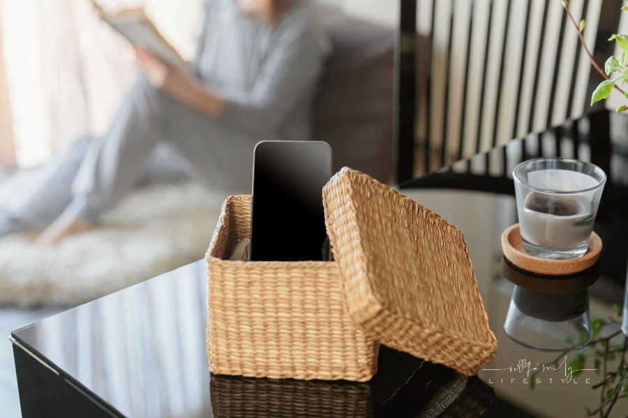 Mental and digital detox concept, phone in wicker box with woman reading in background