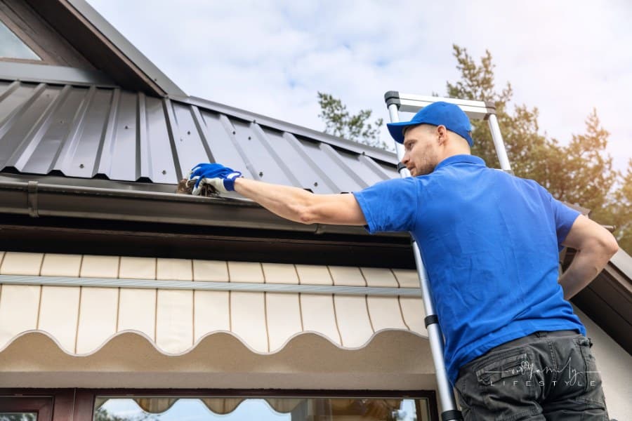 man standing on ladder and cleaning roof rain gutter from dirt