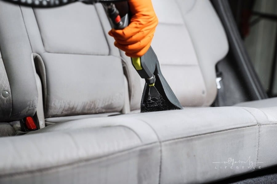 Close-up dry cleaning extractor machine is spraying water and detergent on textile seat inside car. Car dry cleaner is using extraction machine for removing stains and dirt from textile seats.