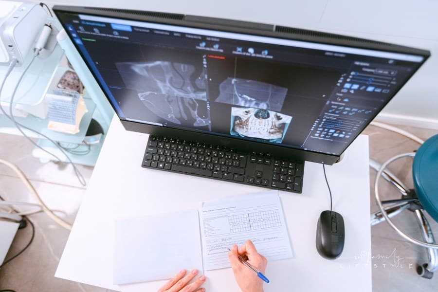 person writing on desktop while looking at x-rays on computer monitor