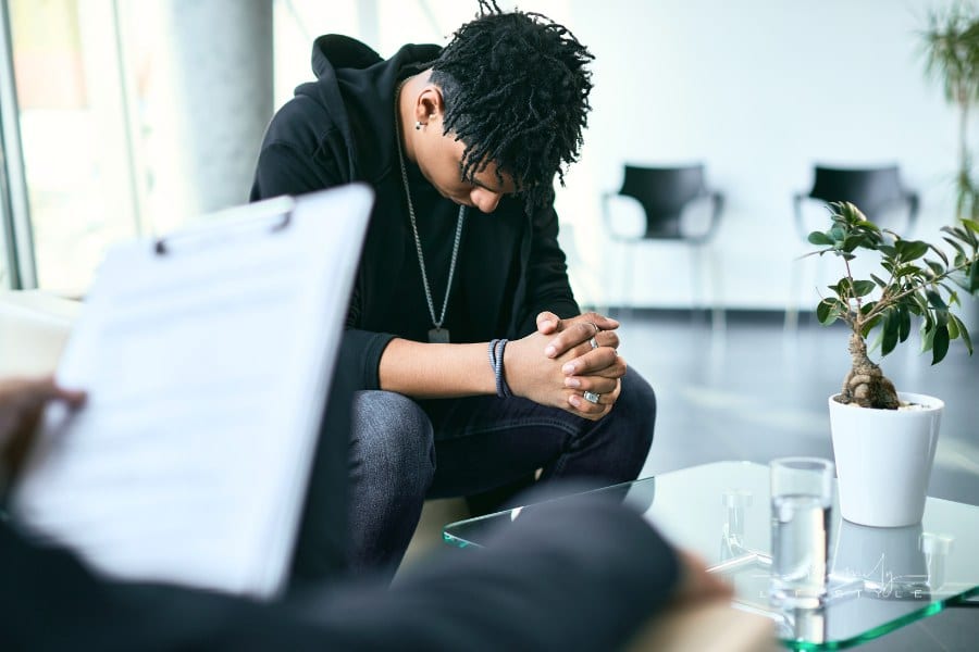 Depressed black teenage boy having counselling with mental health professional.